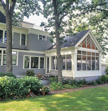 a large gray house with lots of windows on the front and side of it, surrounded by trees