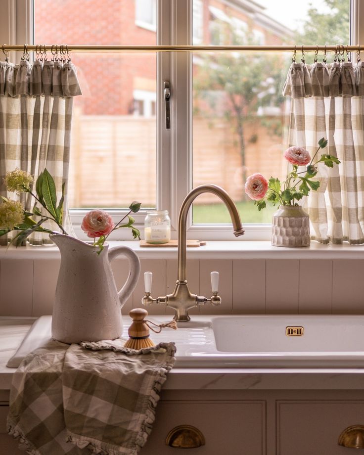 a kitchen sink sitting under a window next to a window sill with flowers on it