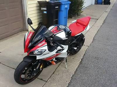 a red and white motorcycle parked on the side of a street next to a blue trash can