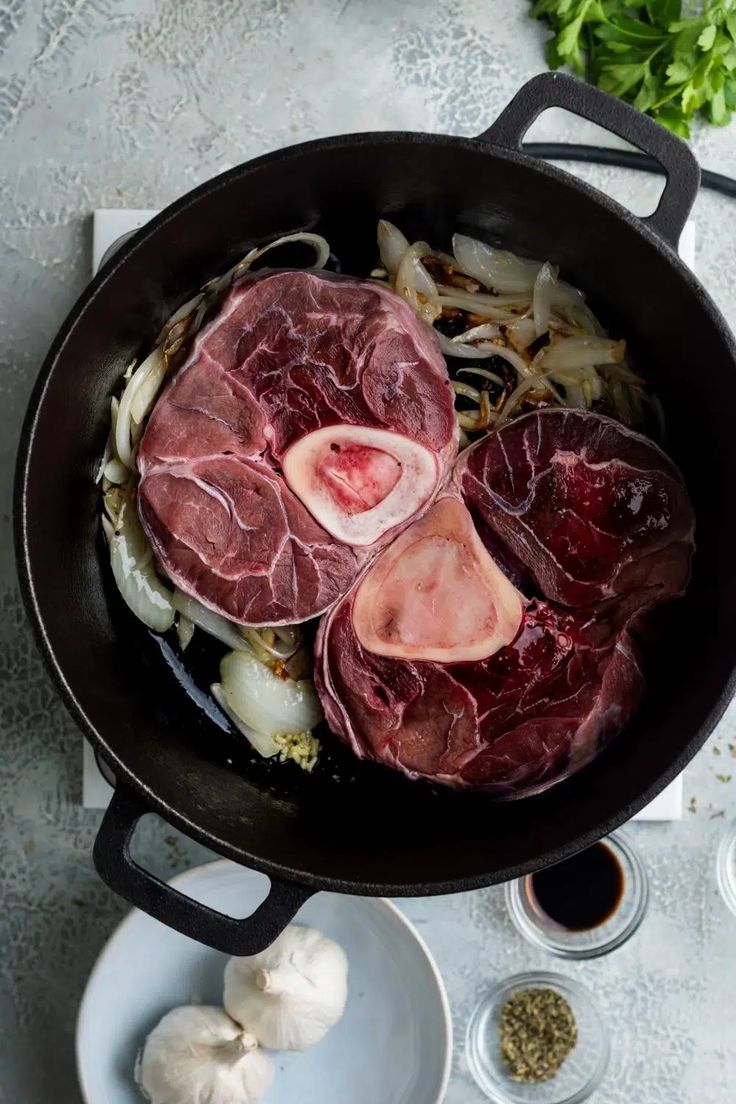 meat and onions cooking in a skillet on a table with spices, garlic and seasonings