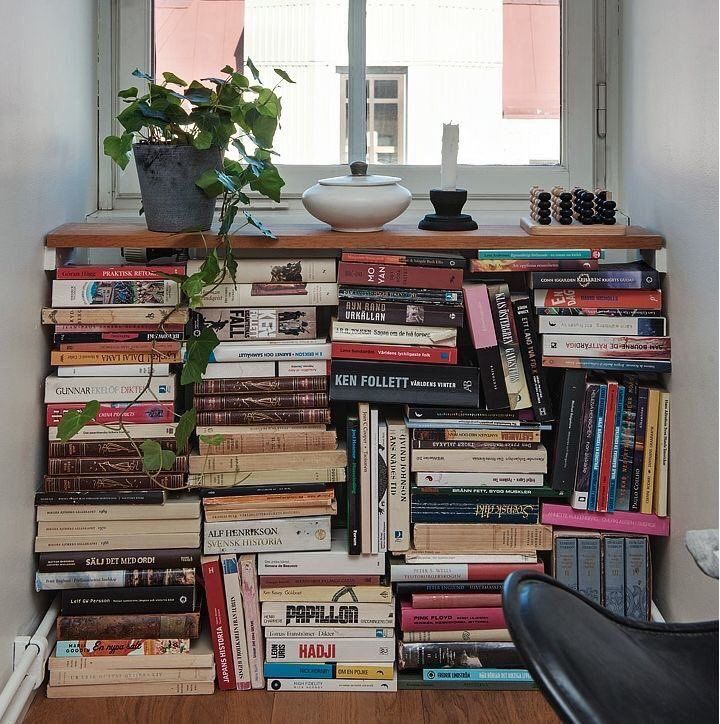 a book shelf filled with lots of books next to a potted plant on top of a window sill