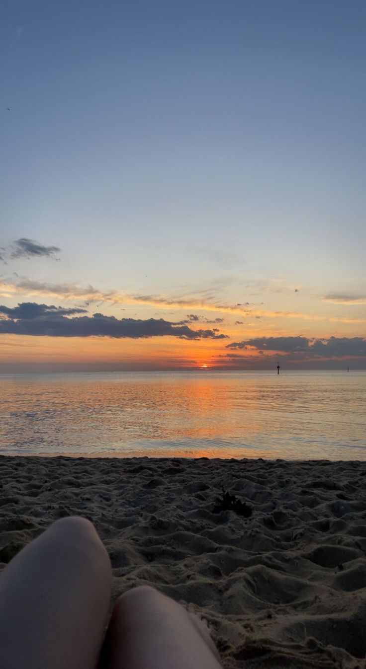 the sun is setting over the ocean and beach with people sitting on the sand looking out at the water