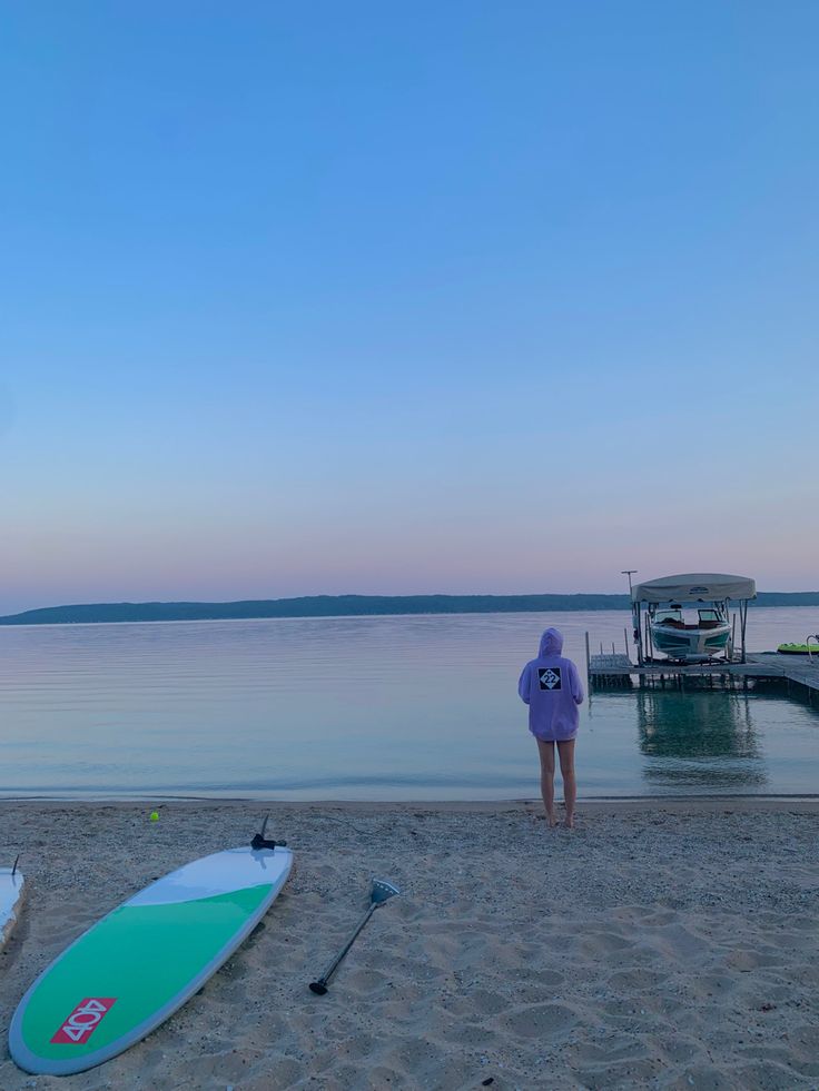 a person standing on the beach next to two surfboards and a boat in the water