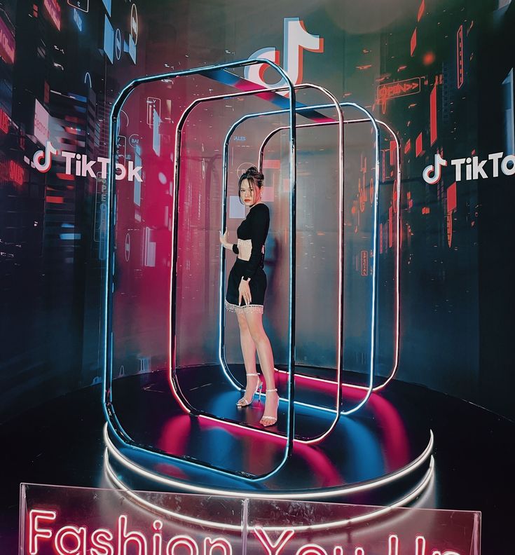 a woman standing in front of a neon display with the words fashion you live on it