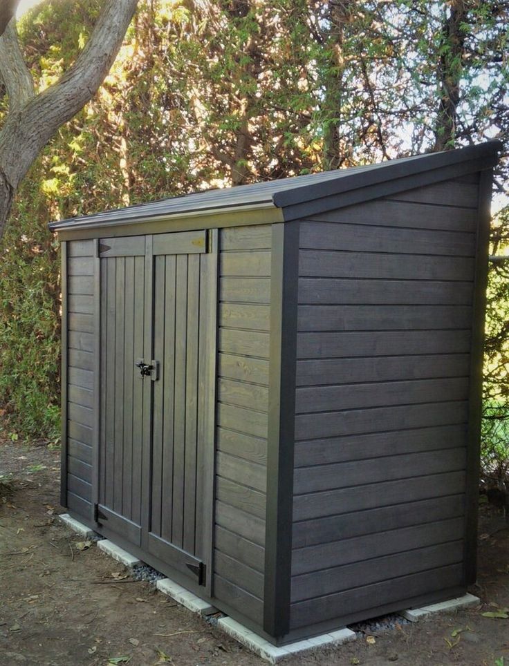 a small storage shed sitting next to a tree