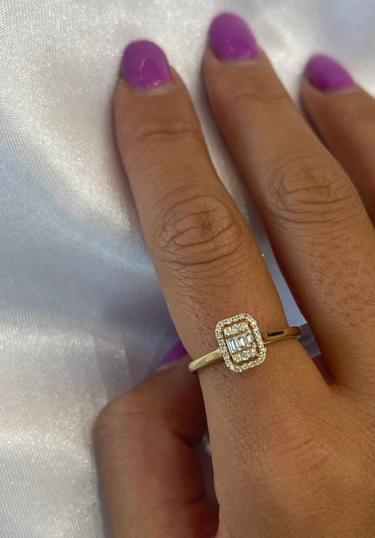 a woman's hand wearing a yellow gold ring with a square shaped diamond in the center