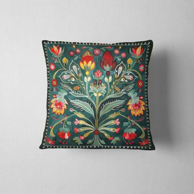 an embroidered pillow with flowers and leaves on the front, sitting against a white wall