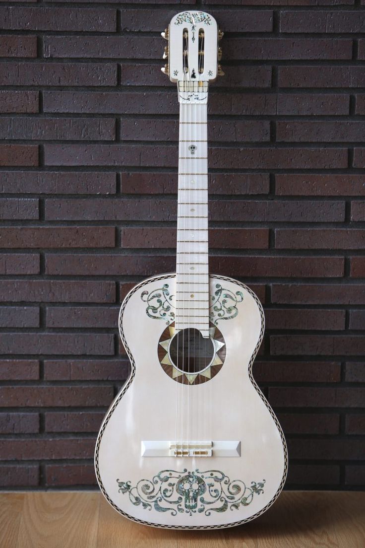 a white guitar sitting on top of a wooden table next to a brick wall and floor