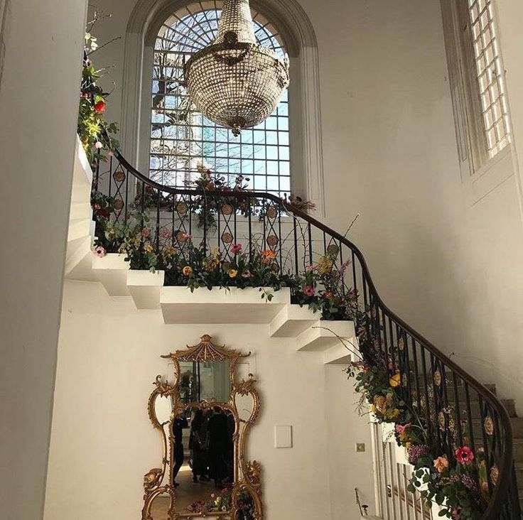 an ornate staircase with flowers on the railing and chandelier hanging from the ceiling