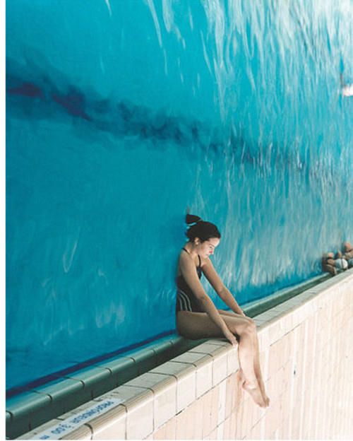 a woman sitting on the edge of a wall next to a swimming pool with blue water