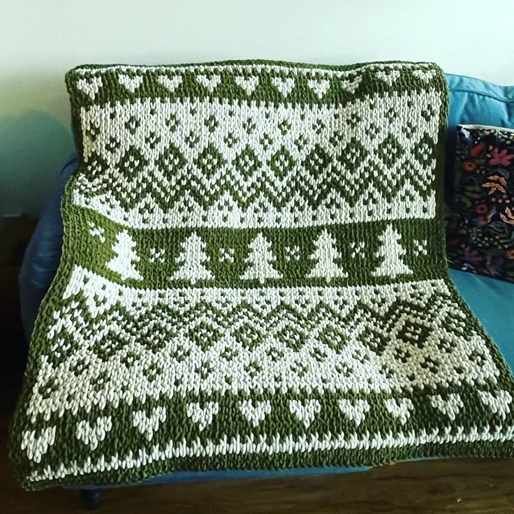 a green and white afghan sitting on top of a blue couch next to a pillow