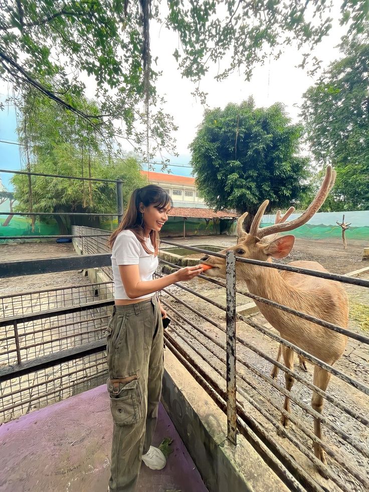 a woman standing next to a fence petting a deer