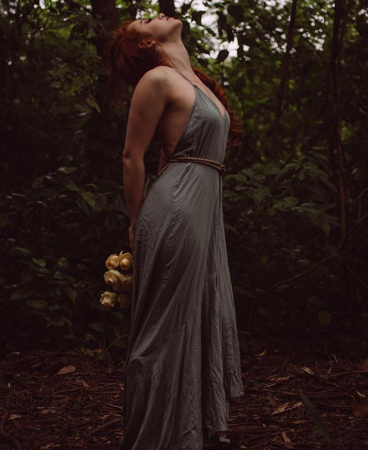 a woman with red hair is standing in the woods wearing a dress and holding an umbrella