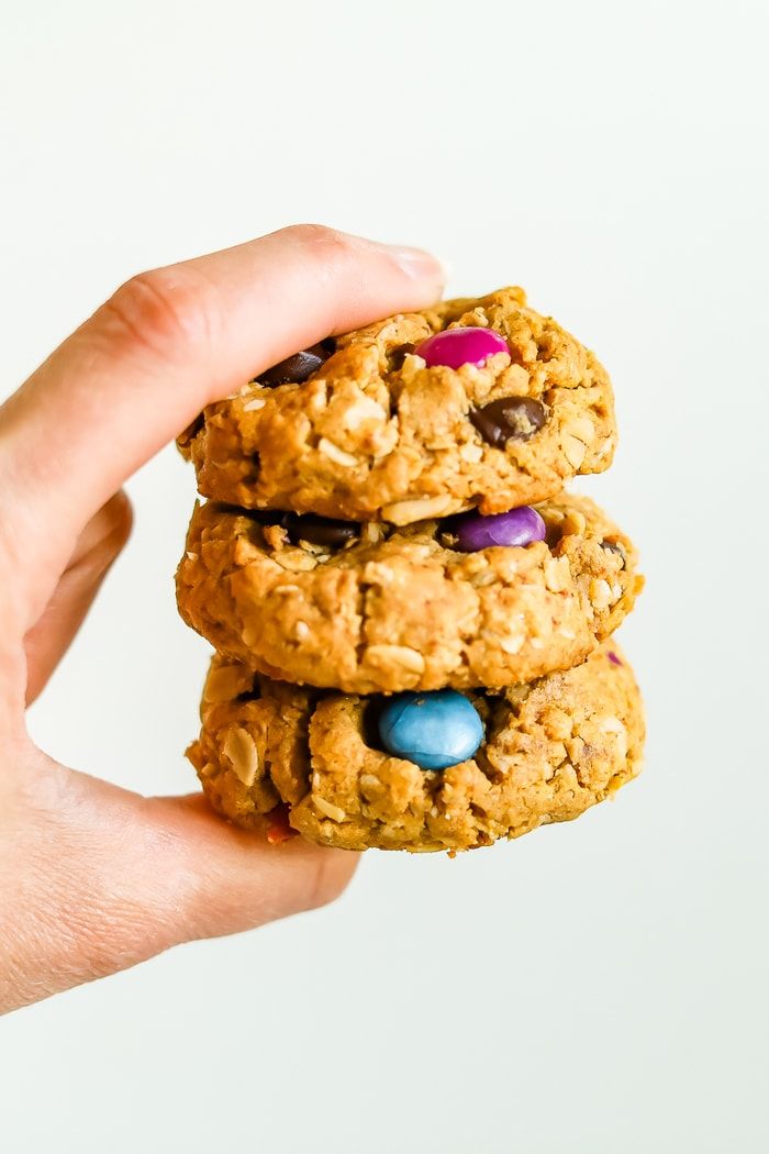 a hand holding three cookies with m & m's on top and candy in the middle