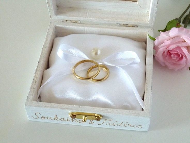 two gold wedding rings sitting in a white box next to a pink rose and diamond ring