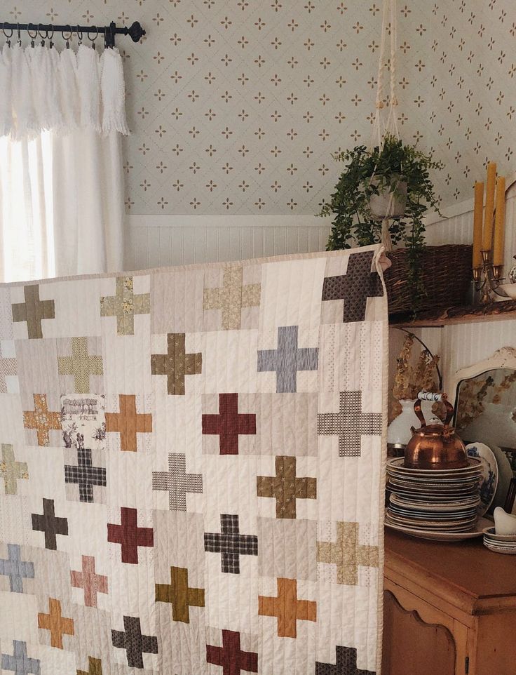 a quilt is hanging on the wall next to a table with plates and dishes in it