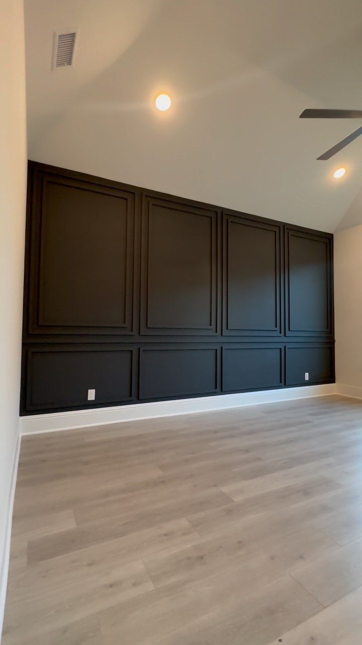 an empty room with dark wood paneling and ceiling fan in the center, surrounded by white walls