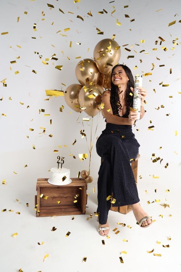 a woman holding a bottle in front of balloons and confetti