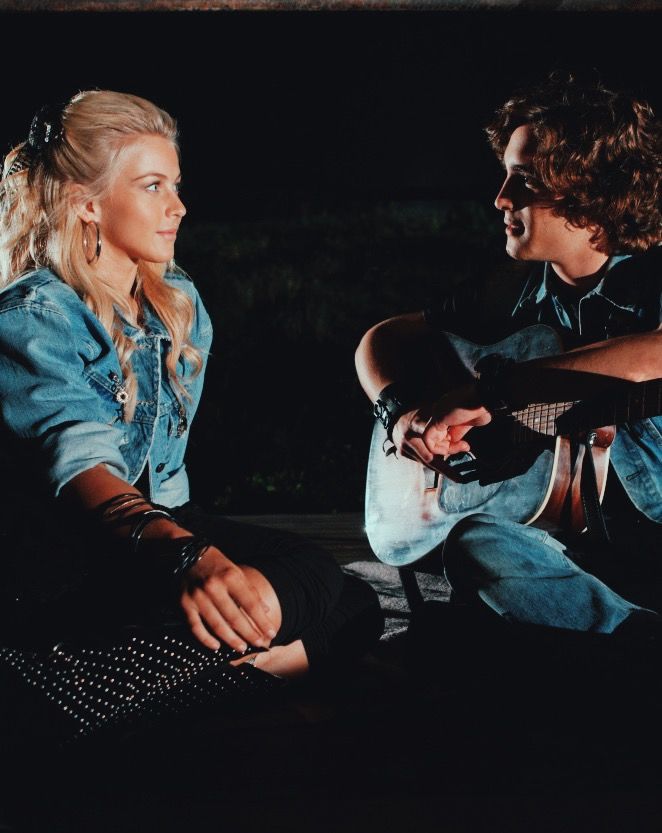 a man and woman sitting next to each other on the ground in front of a black background