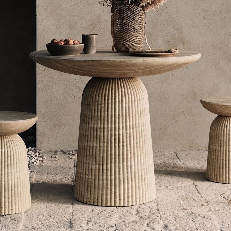 a table and two stools with flowers in the vase next to it on concrete