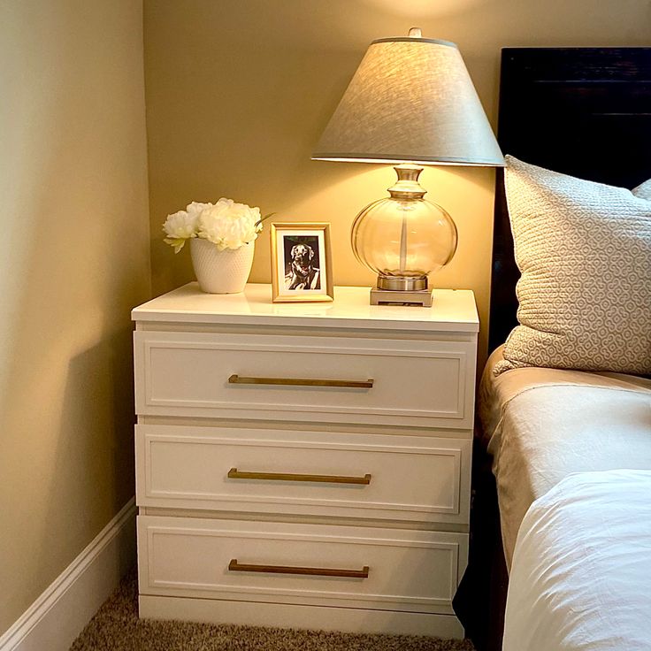 a bedroom with a bed, nightstand and lamp on top of the night stand in front of it