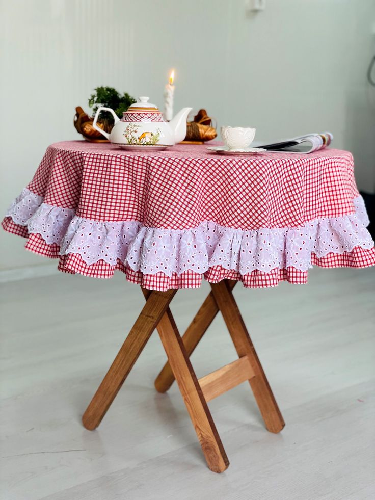 a red and white checkered table cloth with a tea set on it, next to a lit candle