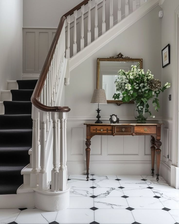 a white staircase with black and white tile flooring next to a wooden console table