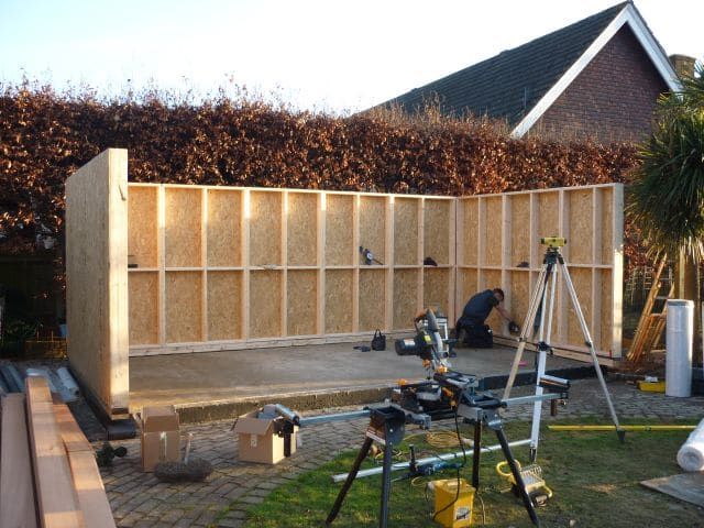 a house being built with wooden walls and construction equipment on the ground in front of it