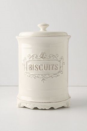 a white cookie jar sitting on top of a table next to a wall with the word cookies printed on it