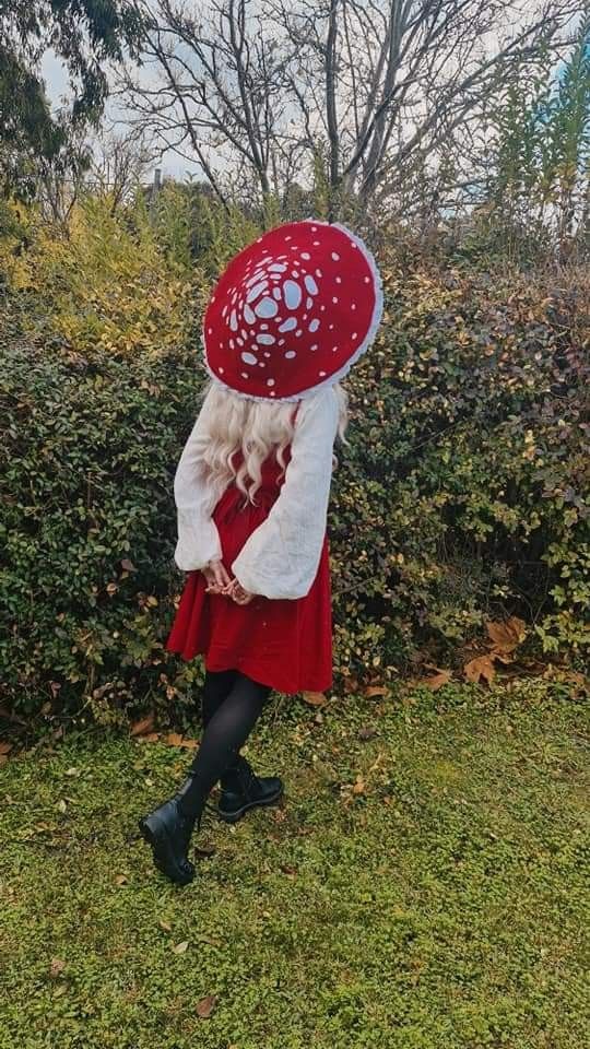 a woman wearing a red and white hat in front of a hedge with her hands on her head