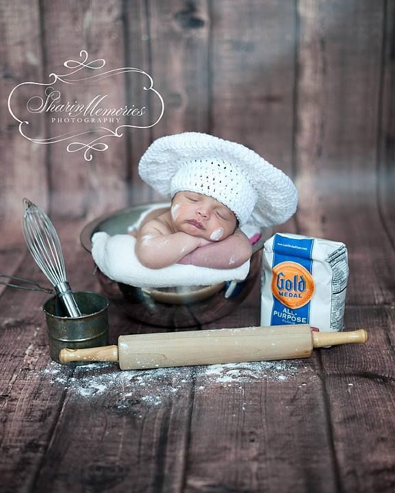 a baby is laying in a bowl next to some food and a whisk