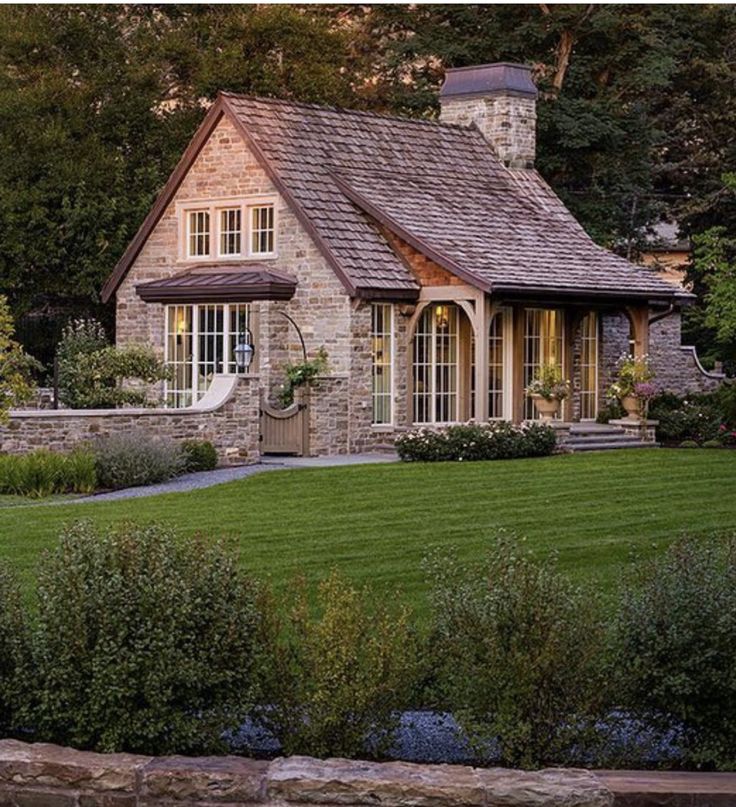 a house that is in the middle of some grass and bushes with trees around it