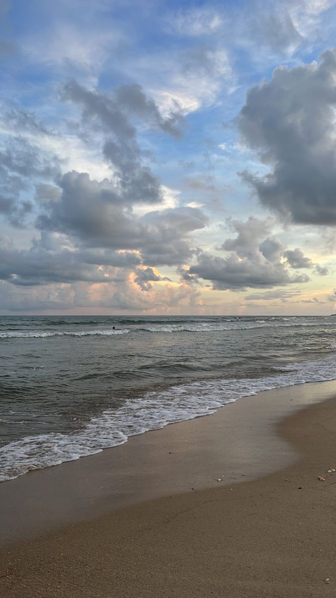 an ocean beach with waves coming in to shore and the sky filled with white clouds