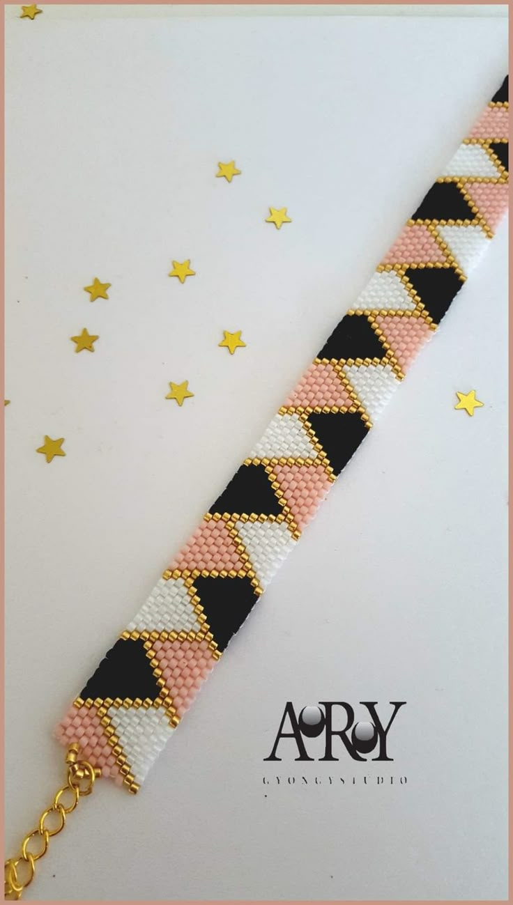 a pink and black bracelet with gold stars on the side, sitting on top of a white background