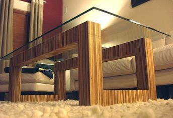 a glass and wood coffee table in front of a couch with white fur on the floor