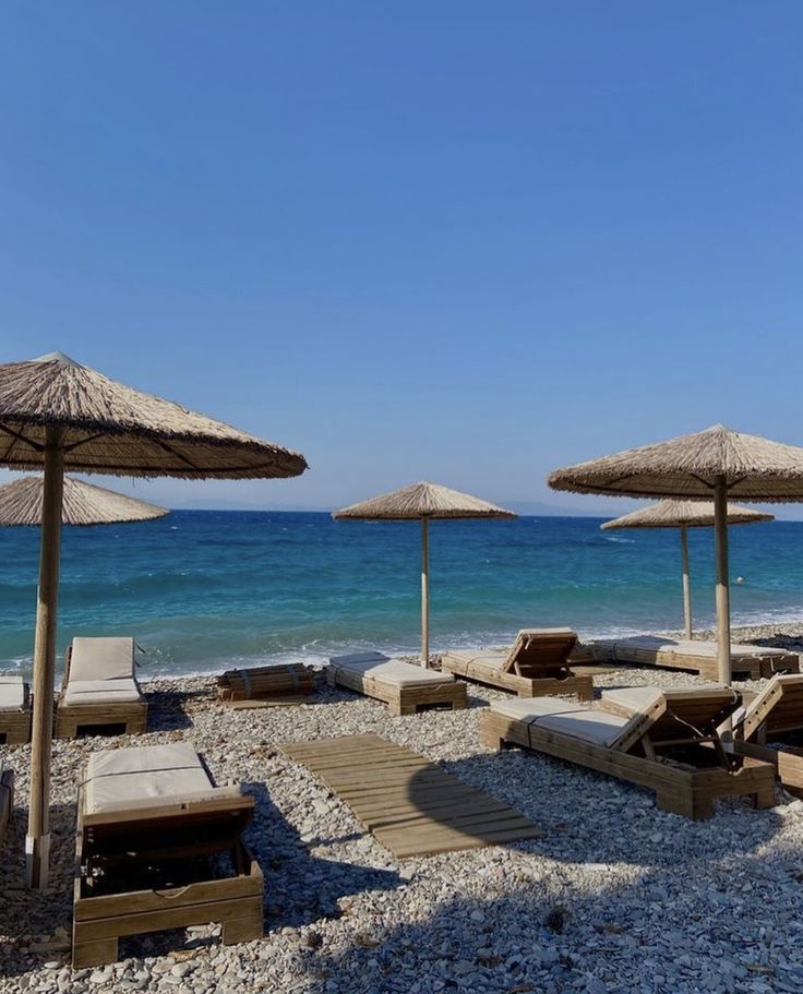 lounge chairs and umbrellas on the beach with clear blue water in the back ground