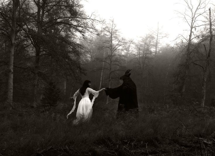 black and white photograph of two people in the woods holding hands with each other,