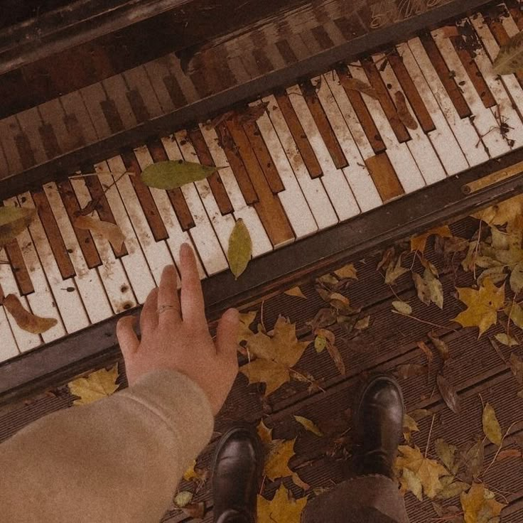 a person standing next to a piano with leaves on the ground near it and their feet