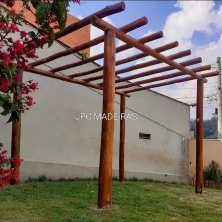 a wooden pergola in front of a building with red flowers on the grass