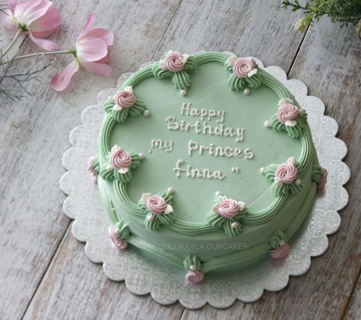 a green birthday cake sitting on top of a white doily next to pink flowers