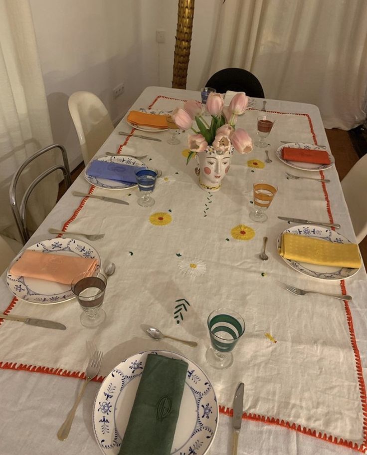 the table is set with plates, silverware and flowers in a vase on it