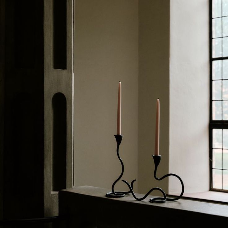 two candles sitting on top of a table next to a window