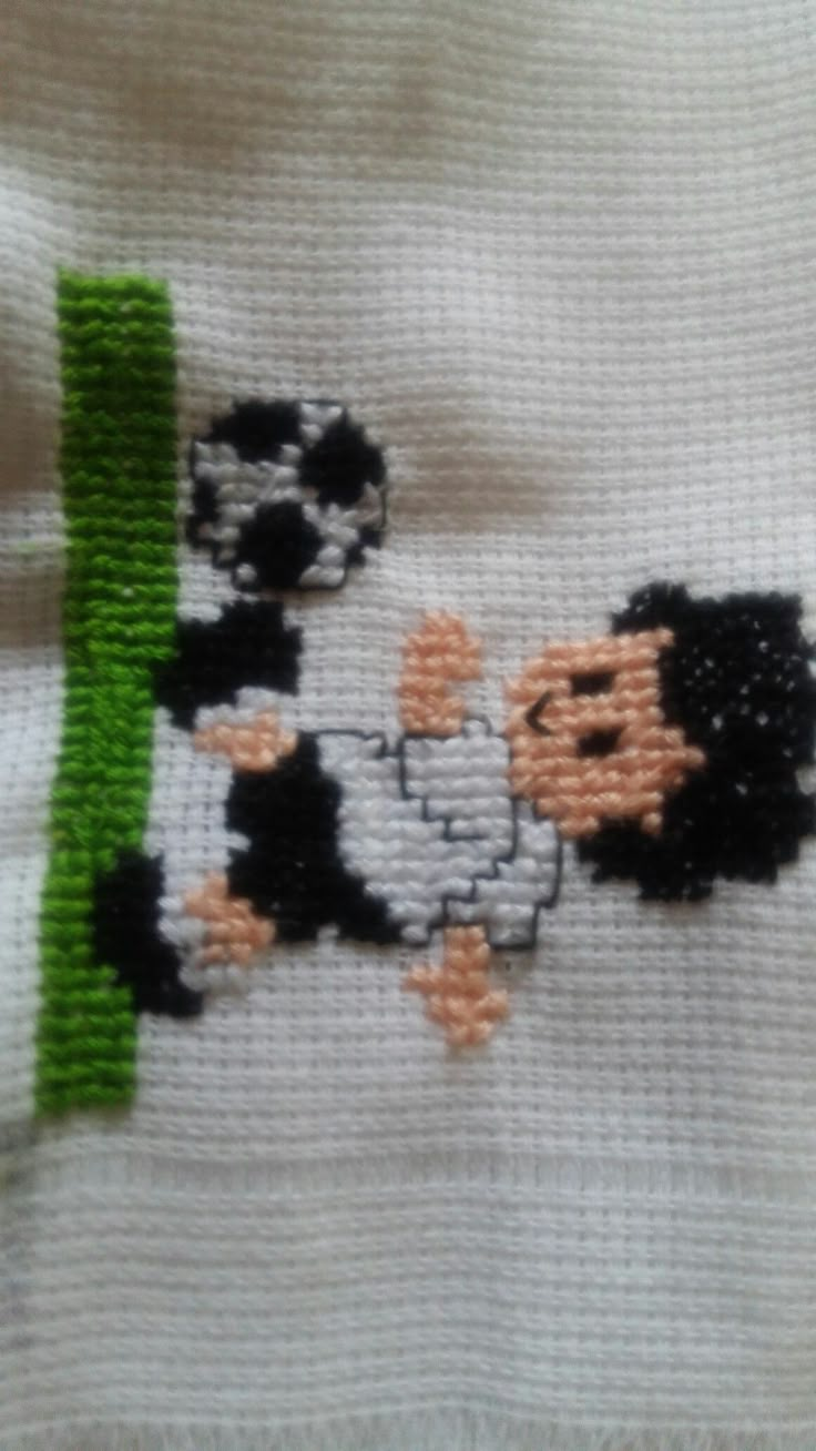 a close up of a cross stitch on a white shirt with black and green trim