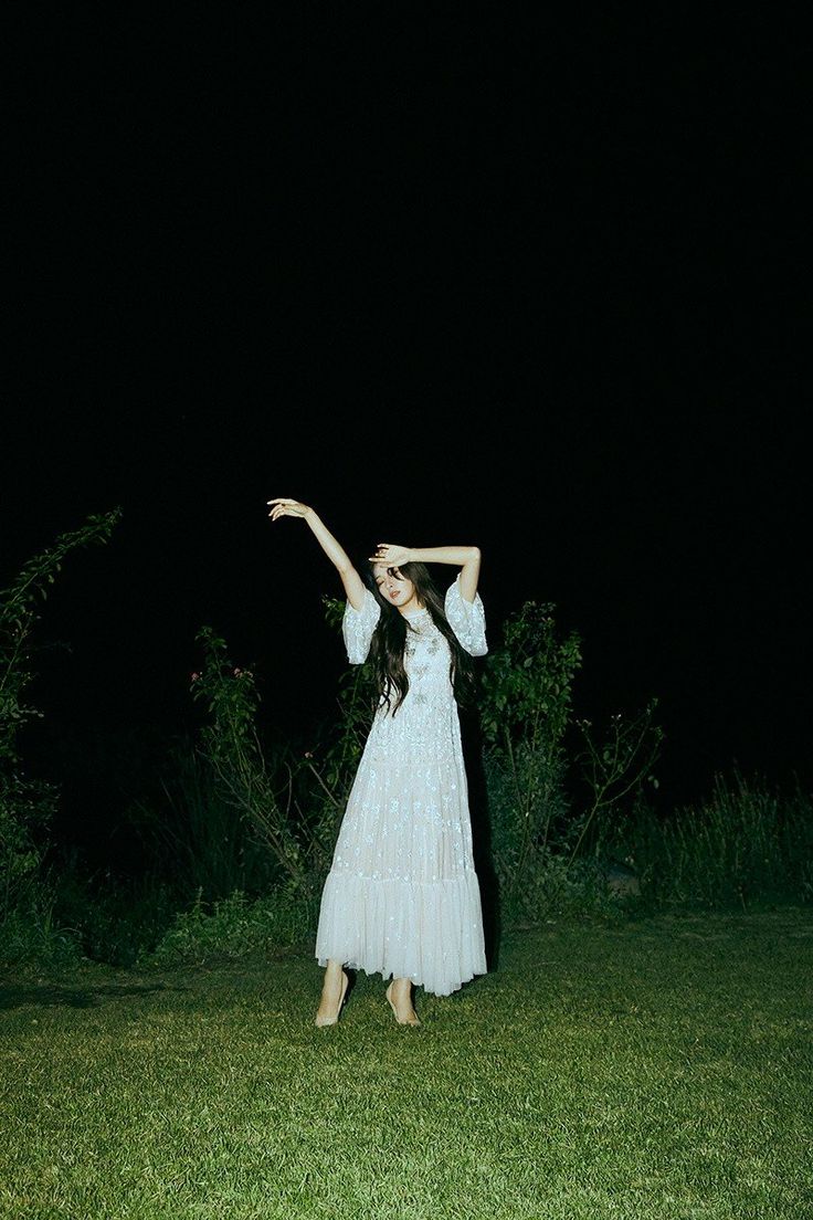 a woman in a white dress is holding her arms up to the sky at night