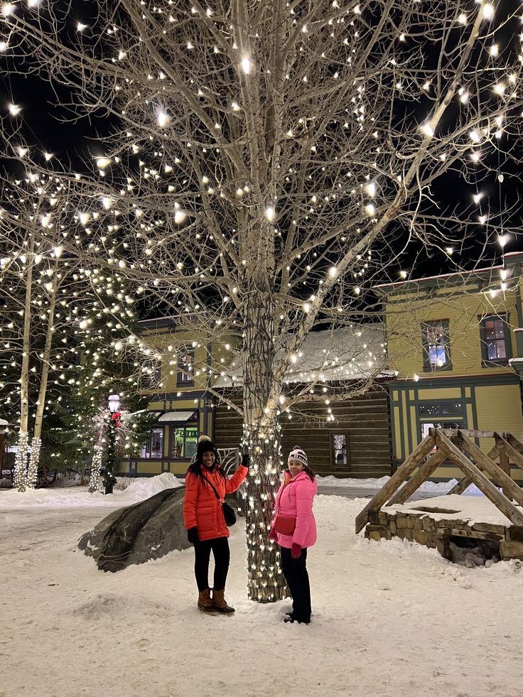 two people standing next to a tree covered in lights