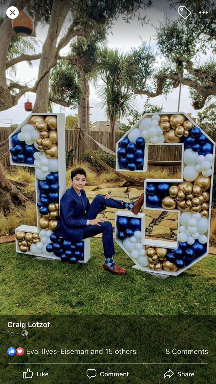 a man sitting on top of a giant letter made out of balloons and balls in the shape of numbers