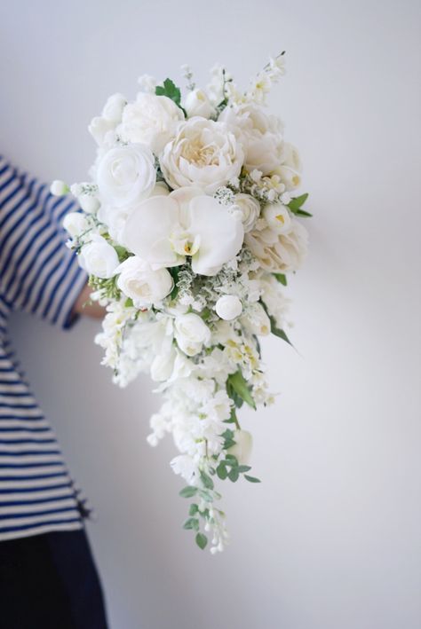 a bouquet of white flowers is held by a woman's hand against a wall