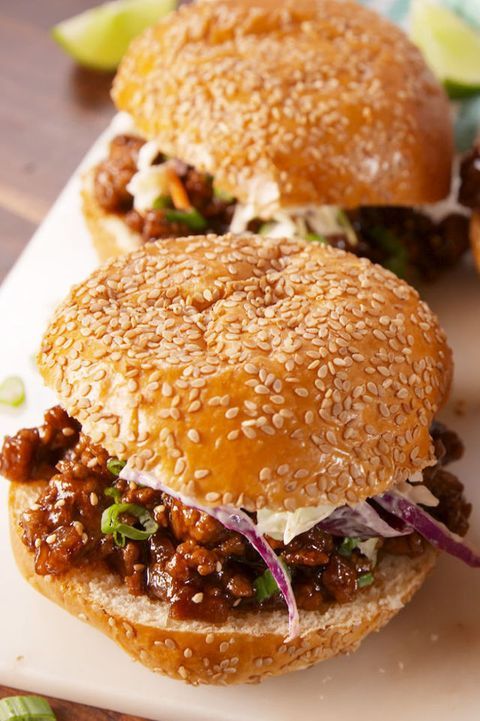 two sloppy joe sandwiches sitting on top of a white cutting board next to lime wedges