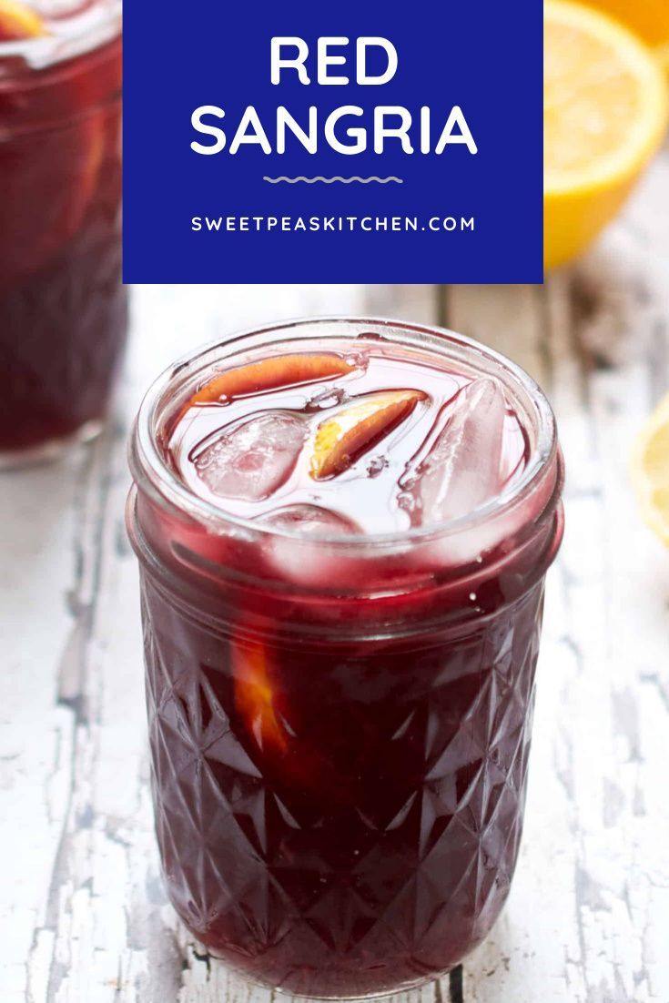 red sangria in a jar with ice and orange slices around it on a white wooden table