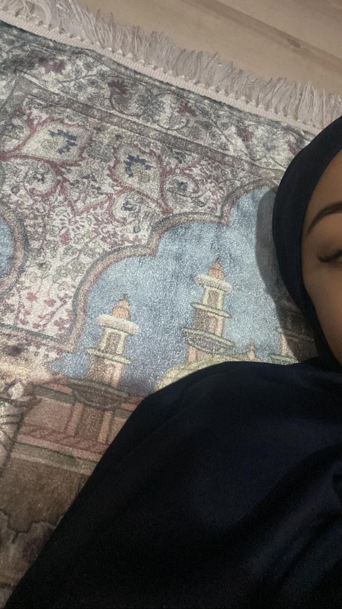 a woman laying on top of a rug with her eyes closed and wearing a headscarf